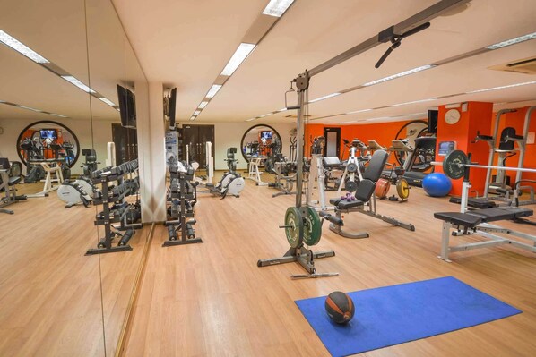 Un gimnasio con diverso equipo de ejercicio, que incluye máquinas de pesas, pesas libres y máquinas de cardio.