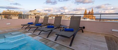 A rooftop pool area with lounge chairs and a view of a historic building.