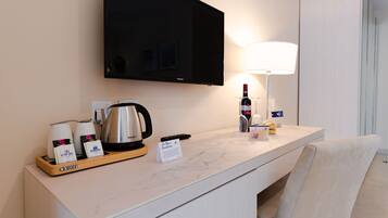 A hotel room with a marble countertop, a flat-screen TV, a coffee maker, a wine bottle, and a lamp.