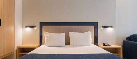 Une chambre d’hôtel moderne avec un grand lit, deux tables de chevet et une tête de lit.