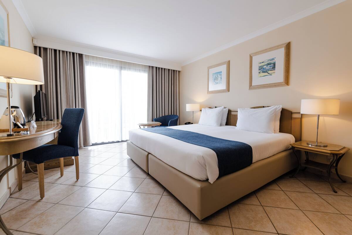 Habitación de hotel con una cama grande, un escritorio con silla, una mesita y dos lámparas.