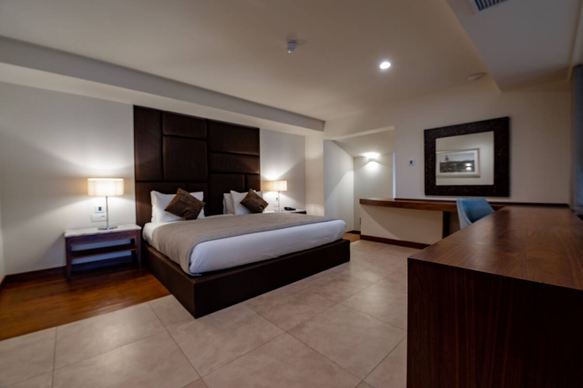 Una habitación de hotel moderna con una cama grande, lámparas de noche, un escritorio y una silla.