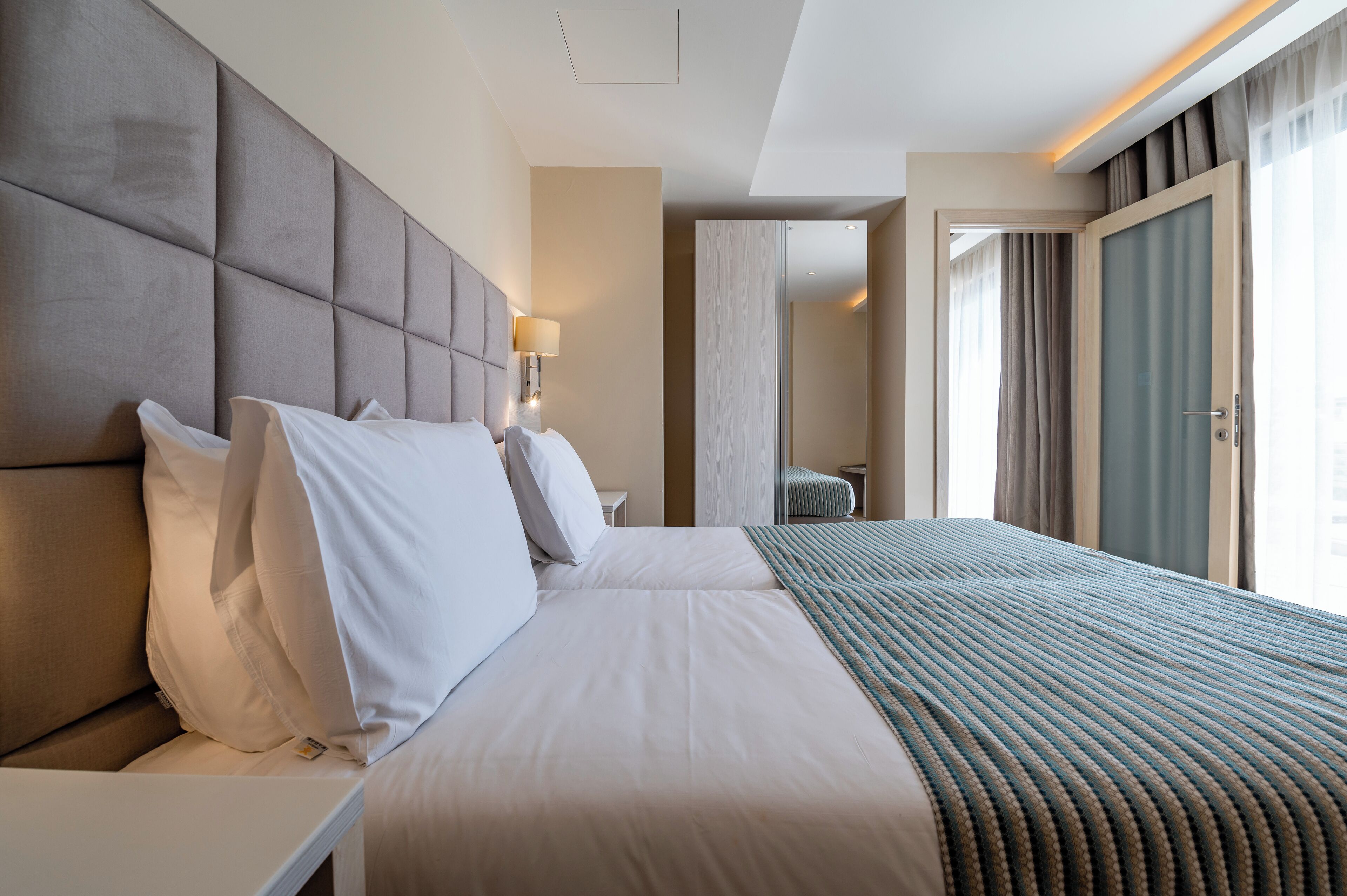 Une chambre d’hôtel avec un grand lit, une tête de lit, une table de chevet avec une lampe et une vue sur l’extérieur par une fenêtre.