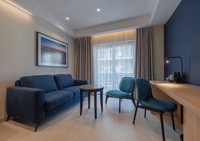 A modern living room with a blue sofa, two chairs, a small round table, and a large window with curtains.