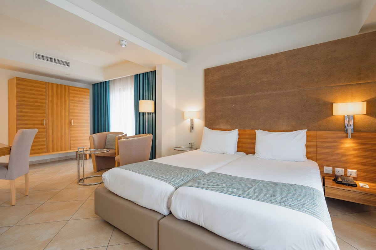A hotel room with a large bed, a desk, a chair, a lamp, and a wall-mounted phone.