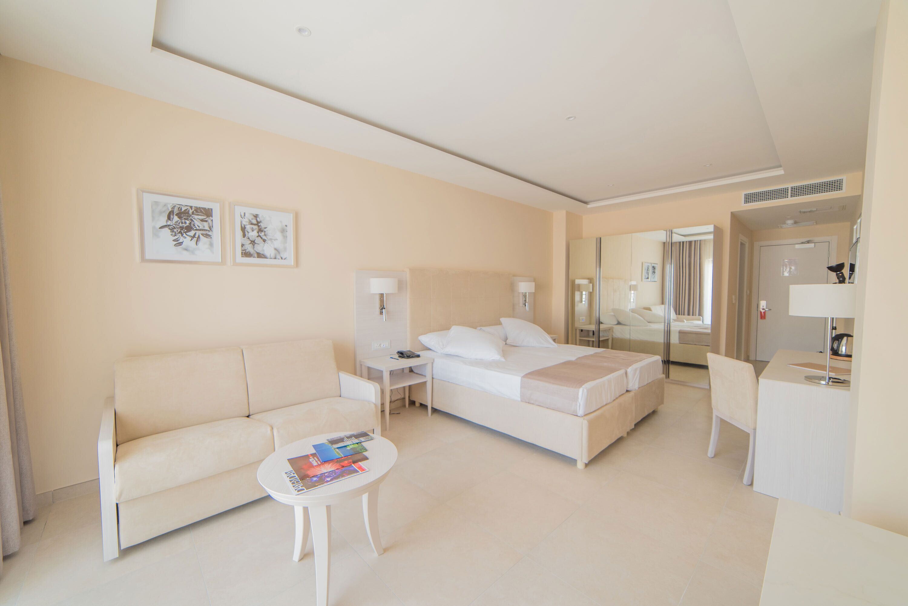 A modern hotel room with a bed, a sofa, a small table, and a desk.