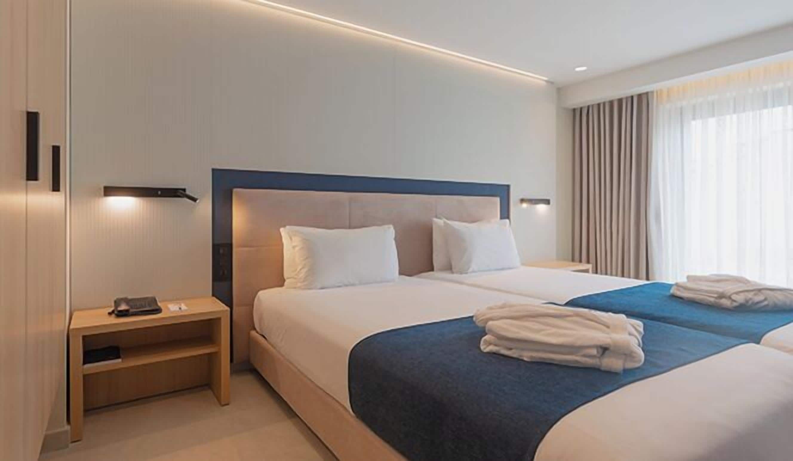 A hotel room with a large bed, two bedside tables, and a window with curtains.