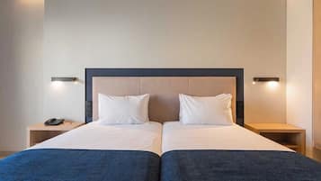 Un lit double recouvert d’une couvre-lit bleu foncé, avec deux oreillers blancs et une tête de lit en bois. Il y a deux tables de chevet, une de chaque côté du lit, et un téléphone noir est posé sur la table de gauche.