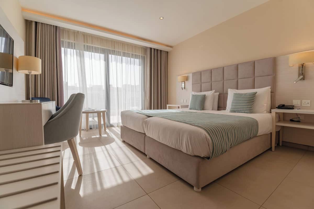 A hotel room with a large bed, a desk, a chair, and a TV.