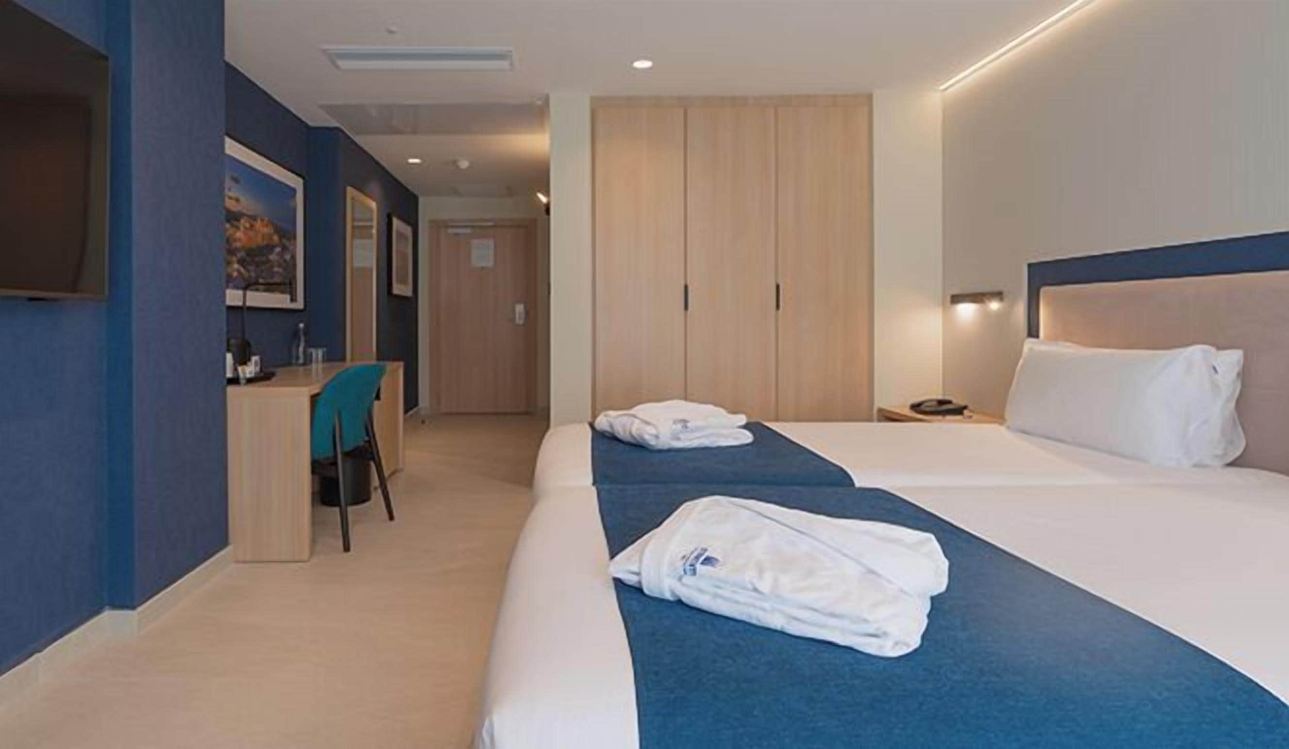 Quarto de hotel com duas camas, uma escrivaninha e um guarda-roupa.