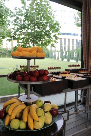 A fruit and dessert buffet with a view of a building and trees in the background.