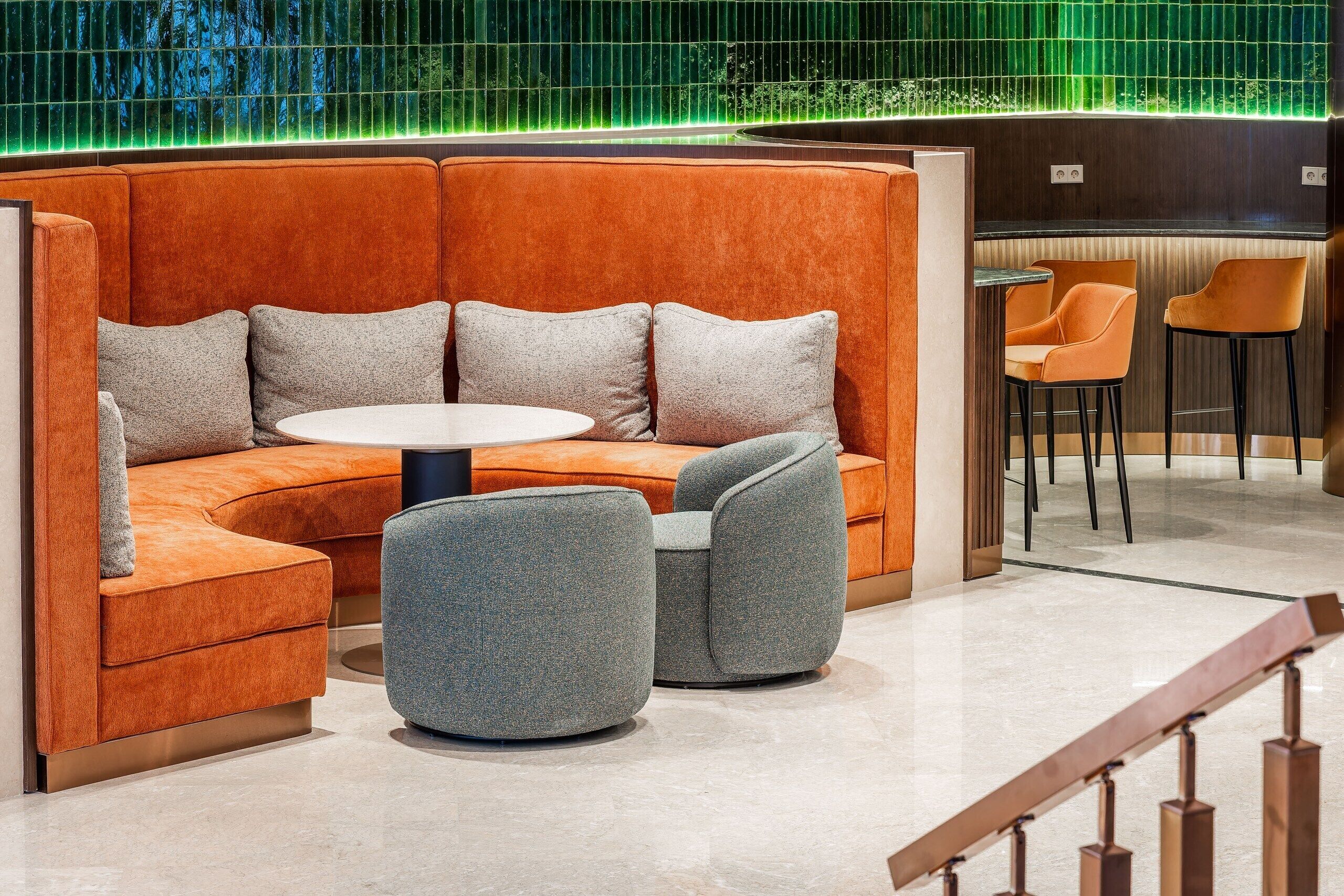 A modern lounge area with a curved orange sofa, grey armchairs, and a round table.