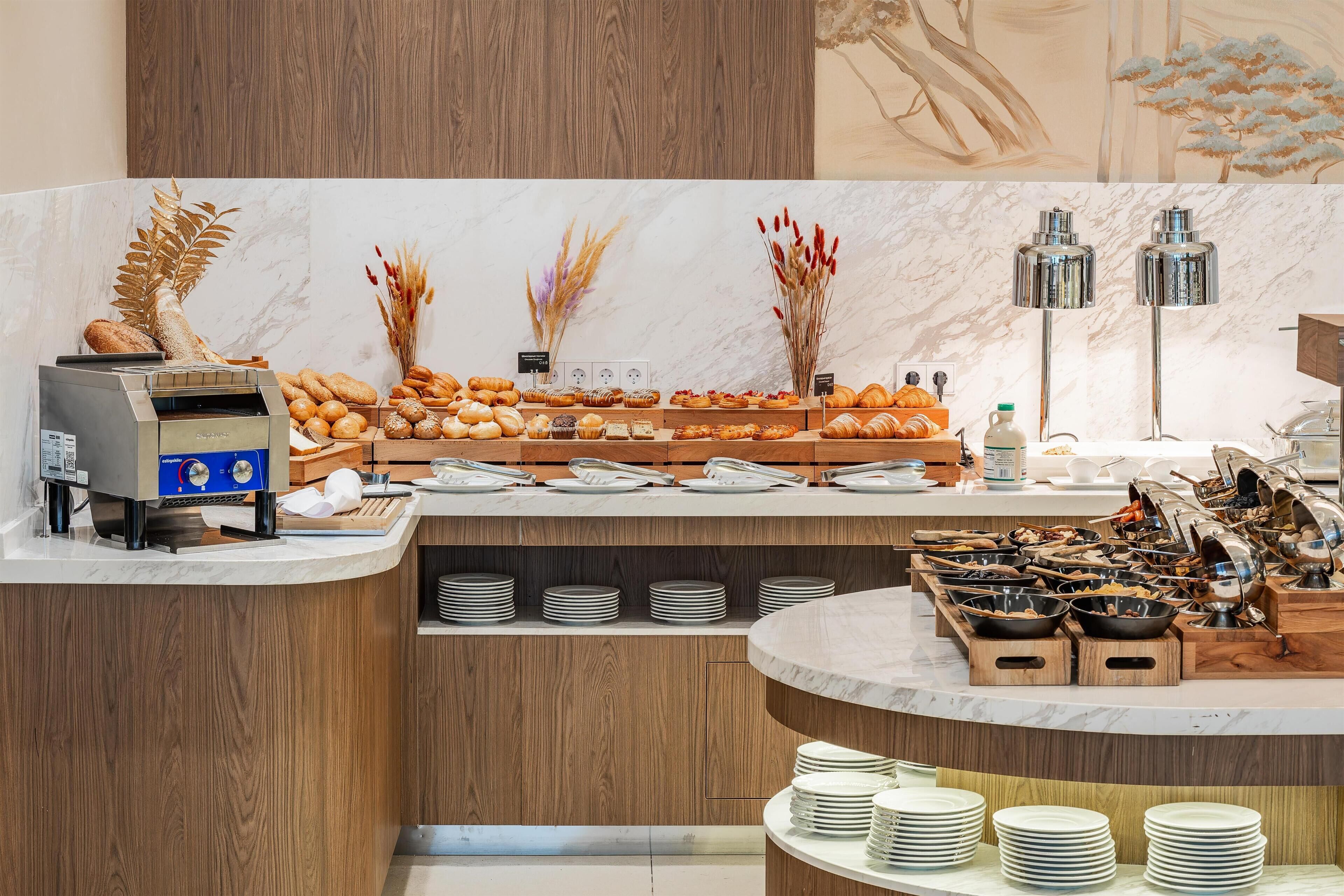 A buffet setup with various food items, a coffee machine, and a decorative wall.