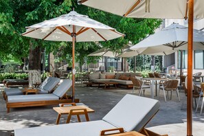 Un espacio al aire libre con sillones, mesas y sombrillas.