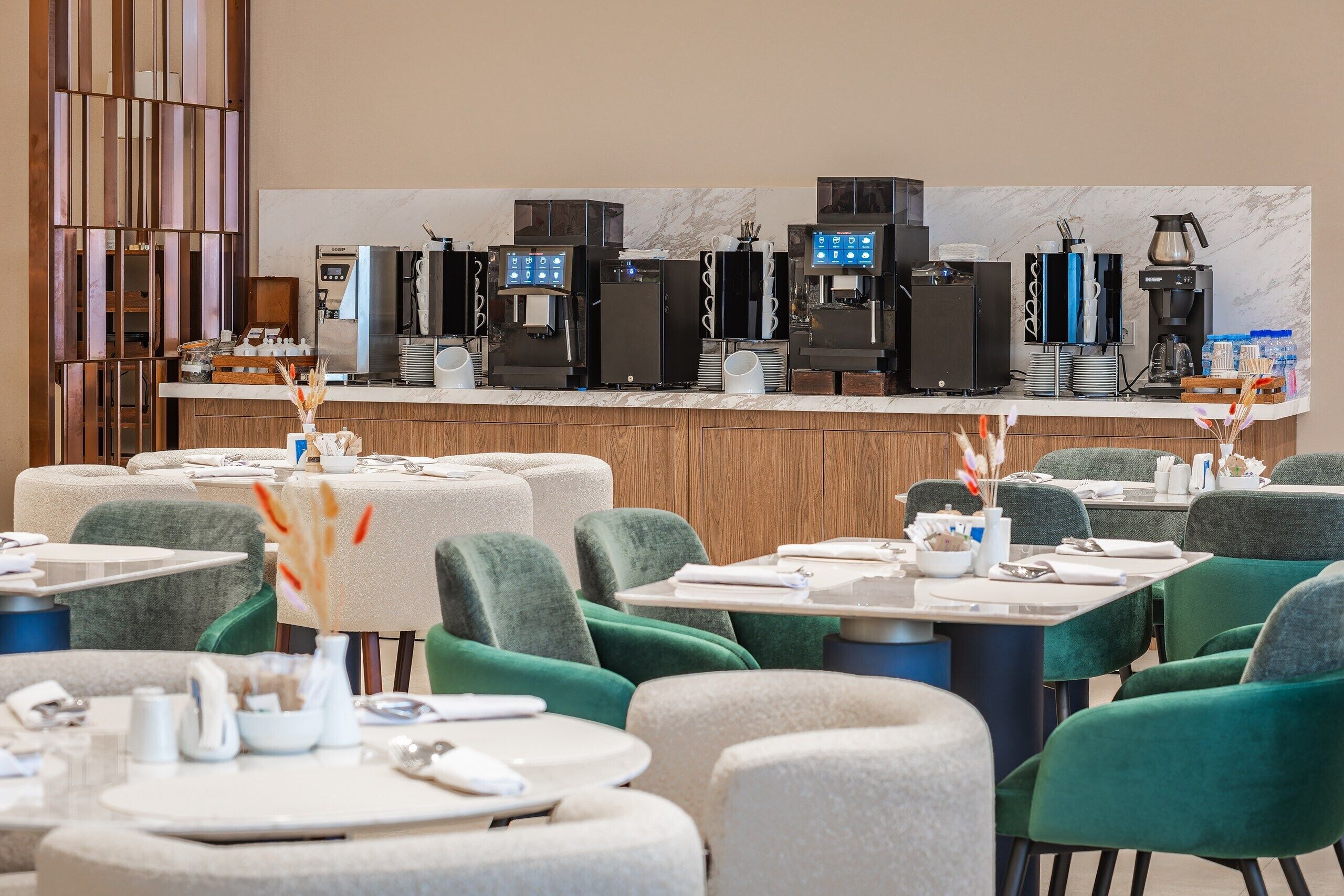 Ein Hotel-Speisesaal mit mehreren Tischen, Stühlen und einer Kaffeestation mit verschiedenen Geräten.