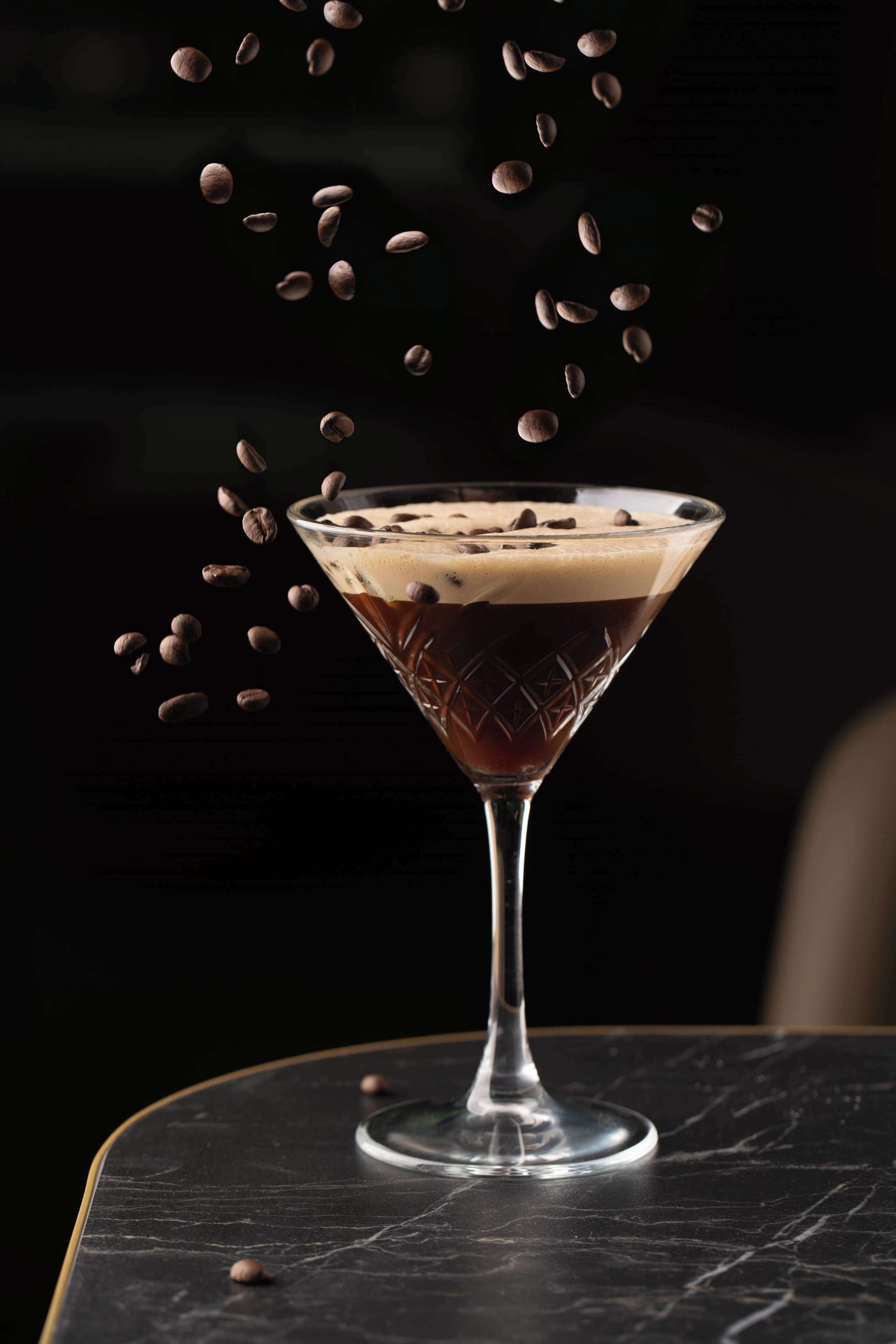 A martini glass with a layered drink on a dark marble table.