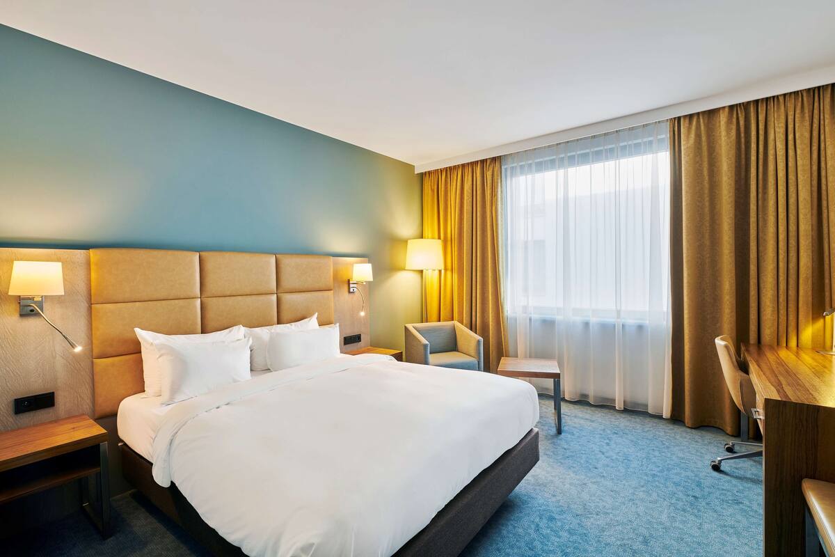 A hotel room with a large bed, bedside tables with lamps, a desk, and a chair.