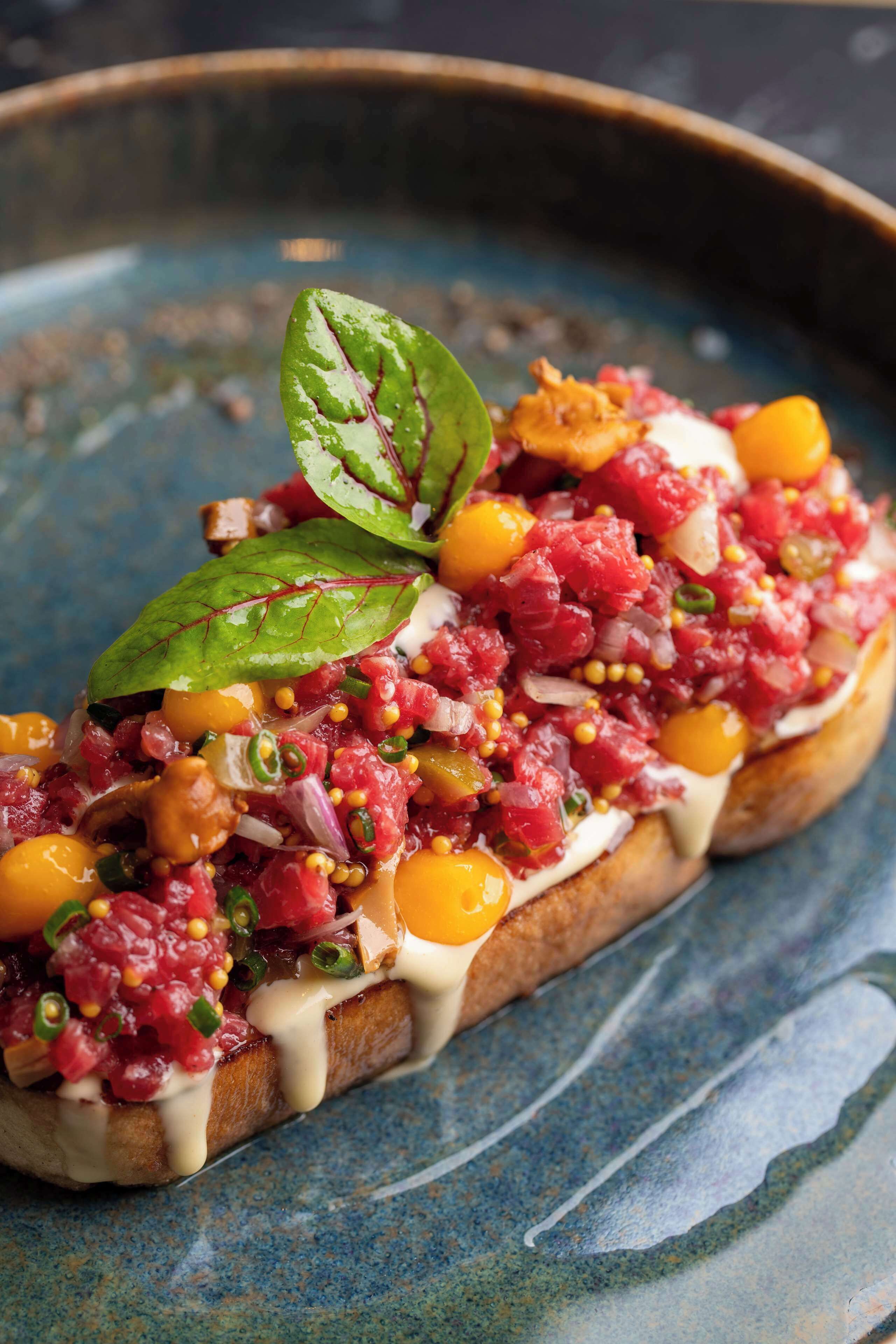 A close-up of a dish with a variety of ingredients on a slice of bread, garnished with a leaf.