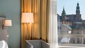 Habitación de hotel con cama, una silla, una lámpara y vistas a un edificio histórico con torres.