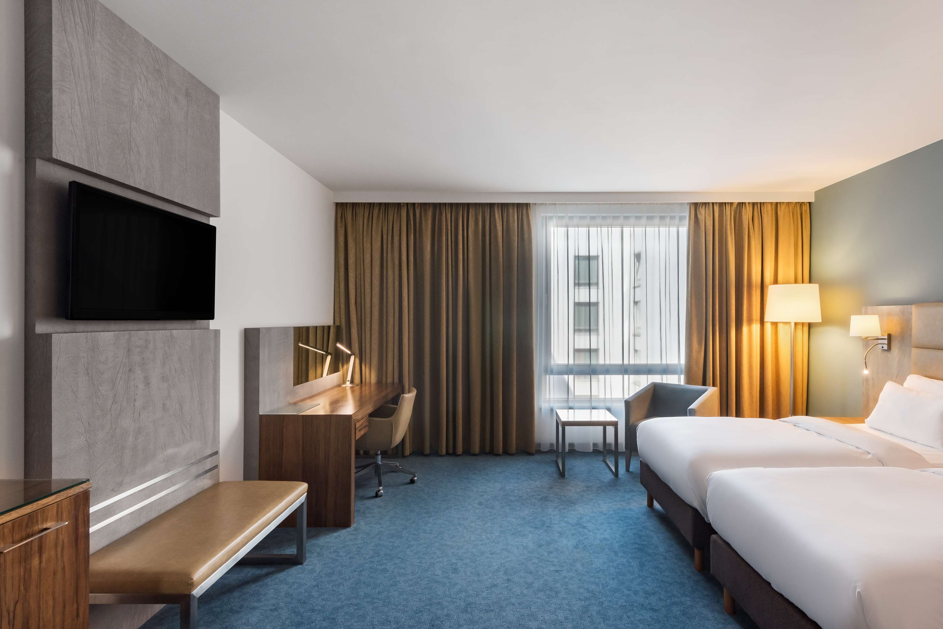 A hotel room with a bed, desk, chair, TV, and a window with curtains.