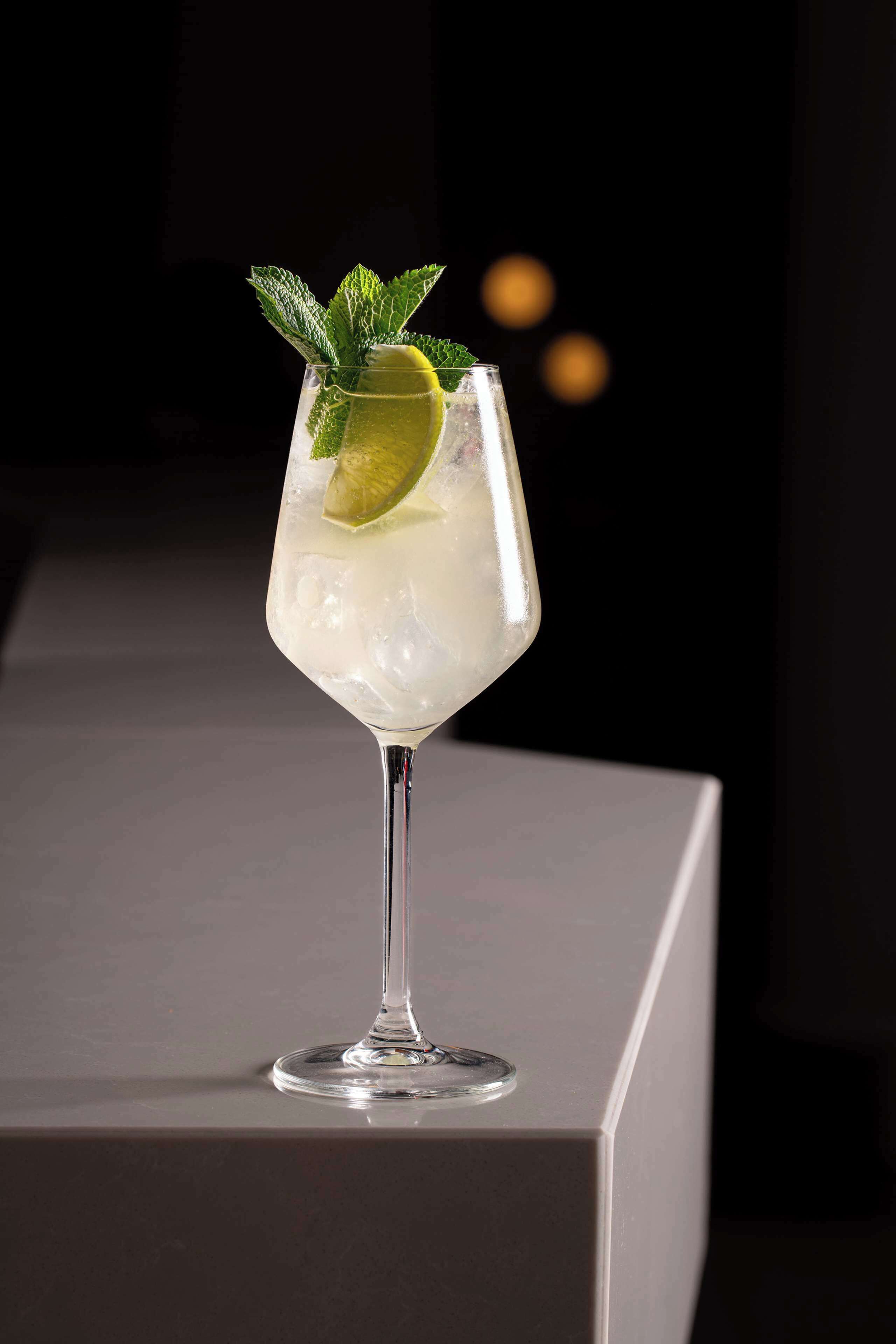 A cocktail glass with ice, lime, and mint garnish on a bar counter.