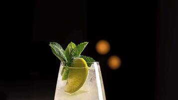 Un vaso de cóctel con hielo, lima y una ramita de menta sobre una barra.