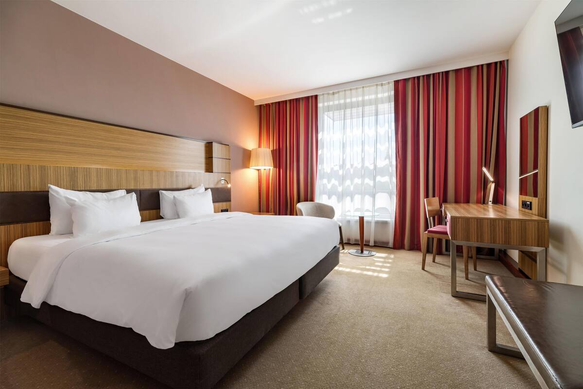 A hotel room with a large bed, a desk, a chair, and a TV.