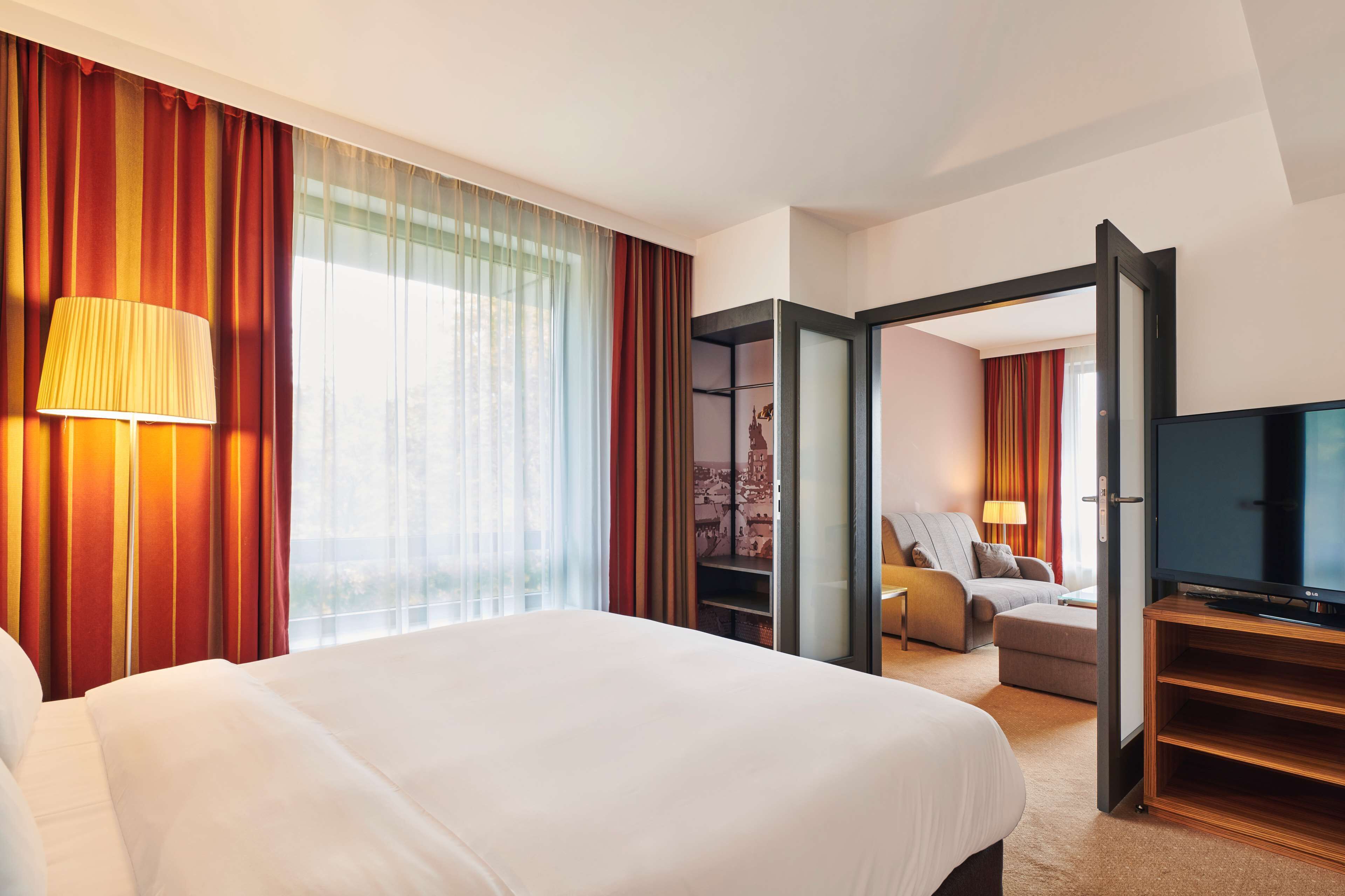 A hotel room with a large bed, a television, a sofa, and a view of the city through the window.