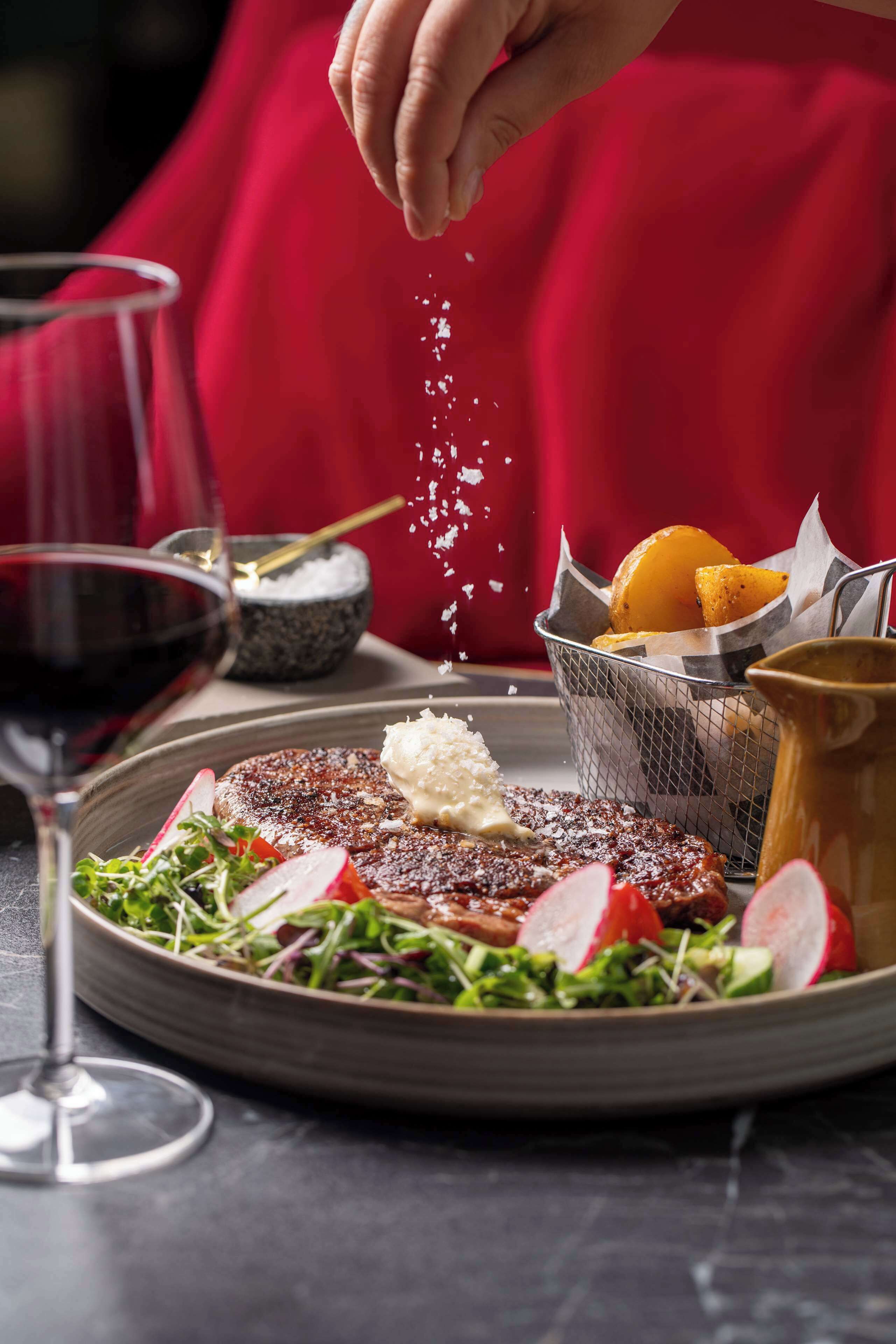 A plate of food with a steak, vegetables, and a glass of red wine.