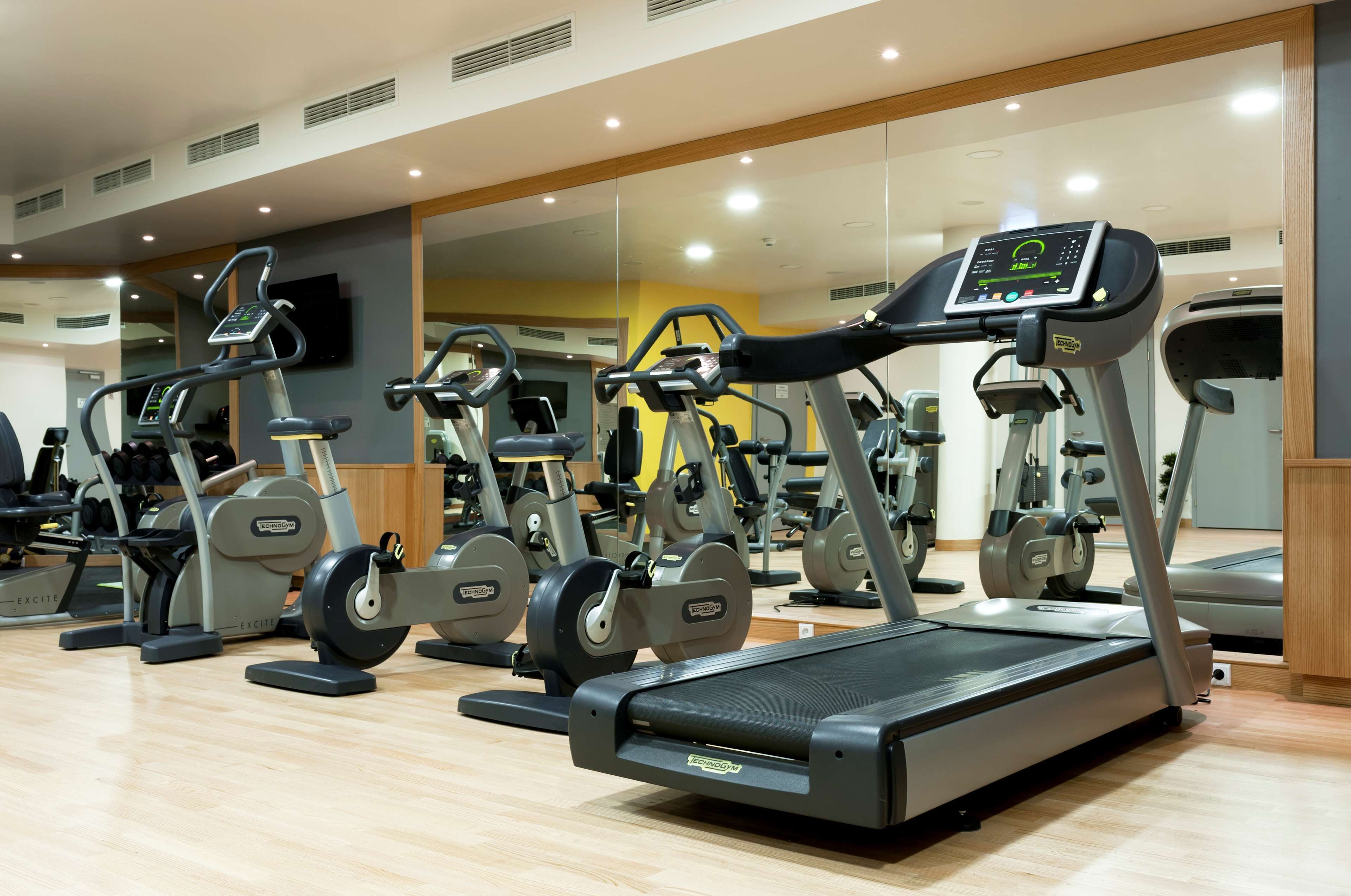 Un gimnasio con diversas máquinas de ejercicio, entre ellas cintas de correr y elípticas, dispuestas en filas.