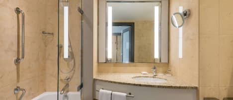Un baño moderno con ducha envuelta en vidrio, una bañera blanca, lavabo con encimera de granito y un espejo grande.