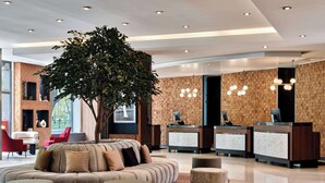Un vestíbulo moderno con recepción, área de descanso y un árbol grande.
