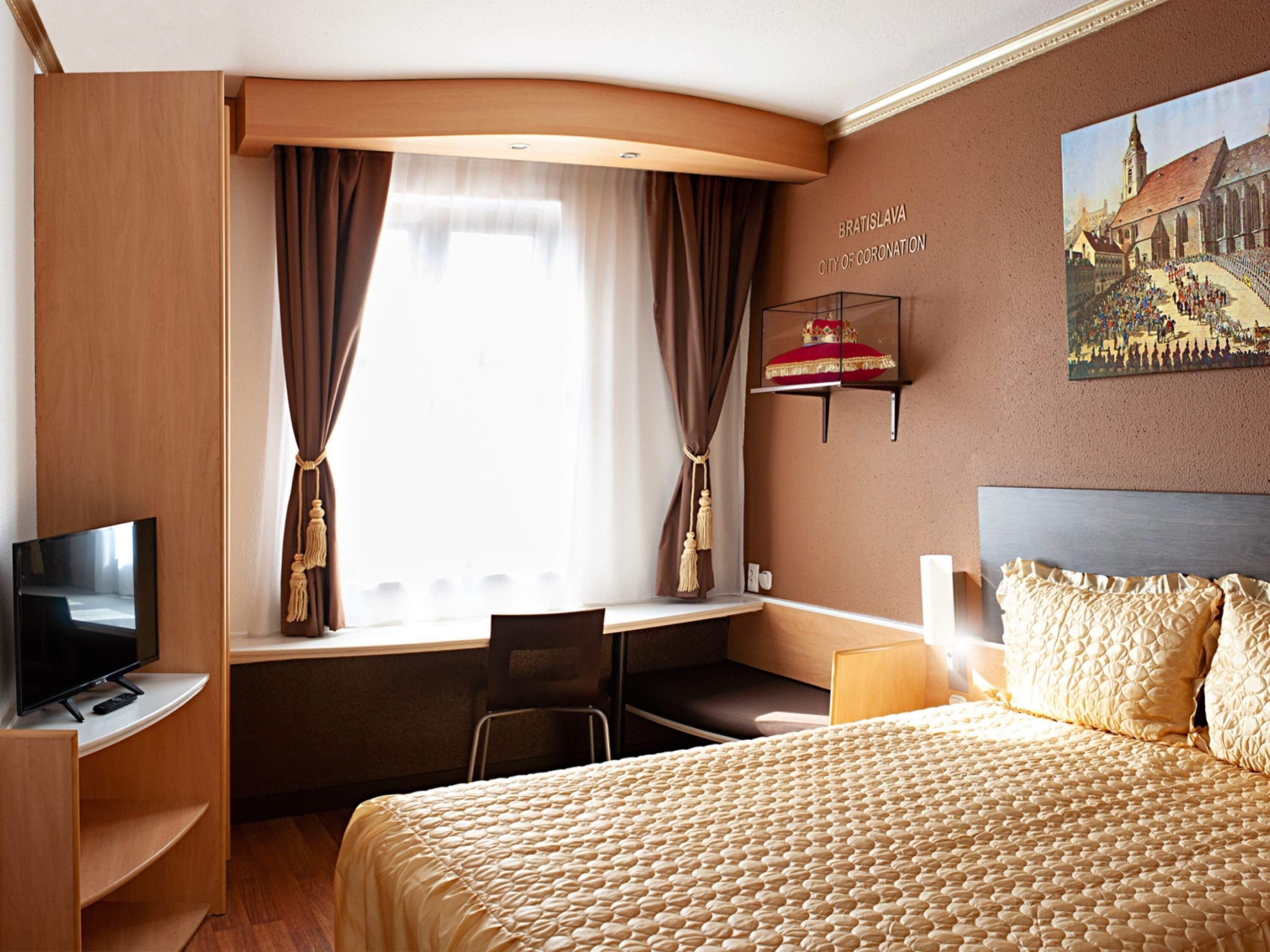 Ein Hotelzimmer mit Bett, Schreibtisch, Stuhl, Fernseher und einem Gemälde von Bratislava.