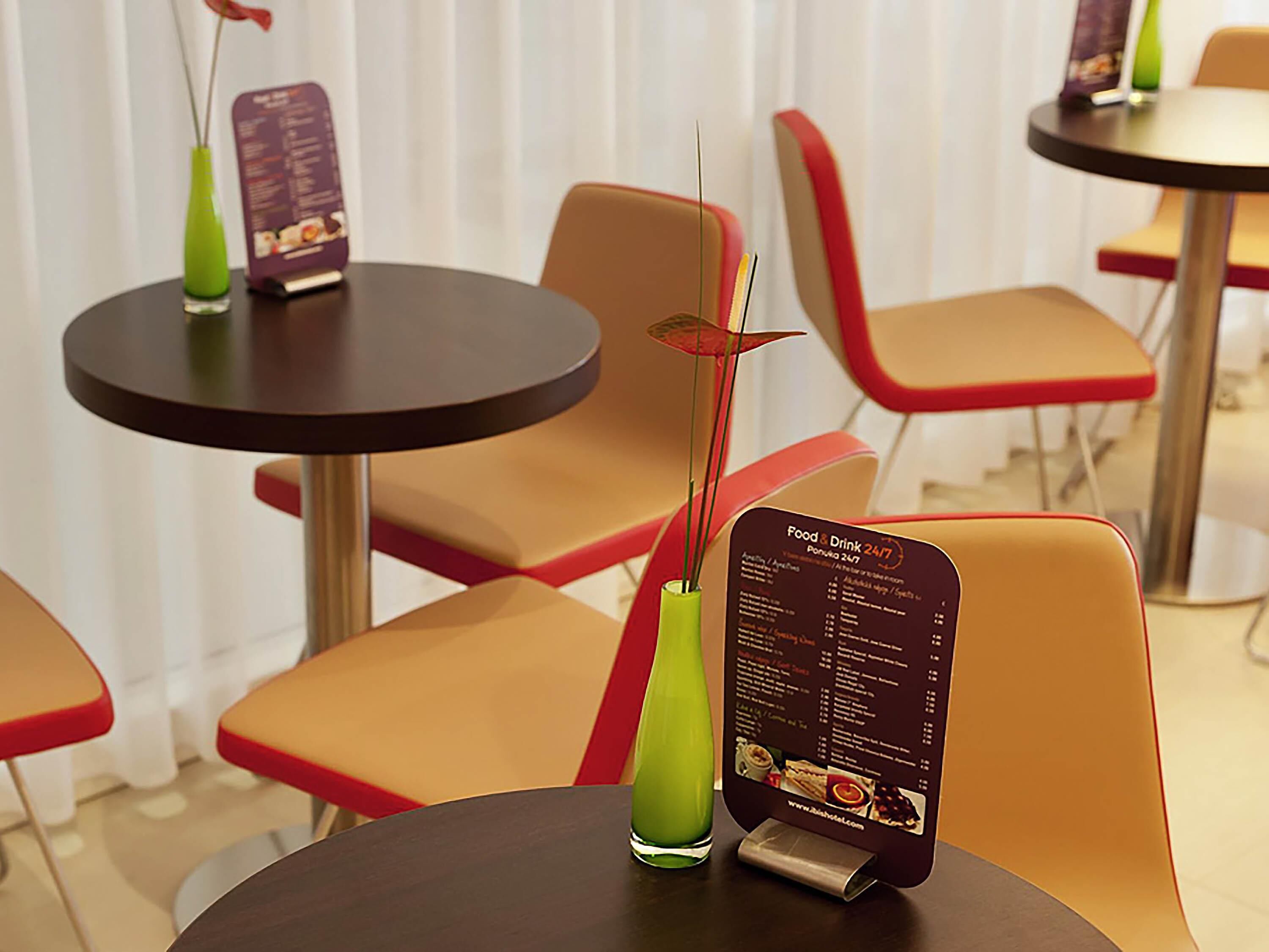 A restaurant interior with round tables, red and beige chairs, and a menu stand displaying food and drink options.