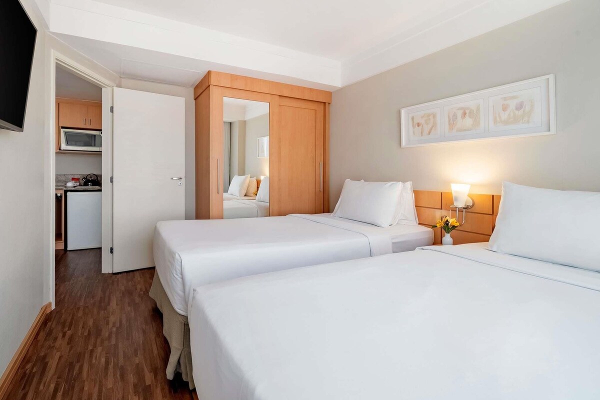 A hotel room with two beds, a kitchenette, and a bathroom.