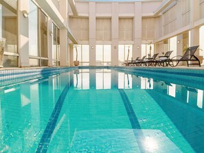 An indoor swimming pool with clear water, sunlit interior, and lounge chairs along the poolside. - Mercure Guarulhos Aeroporto Hotel (Guarulhos)