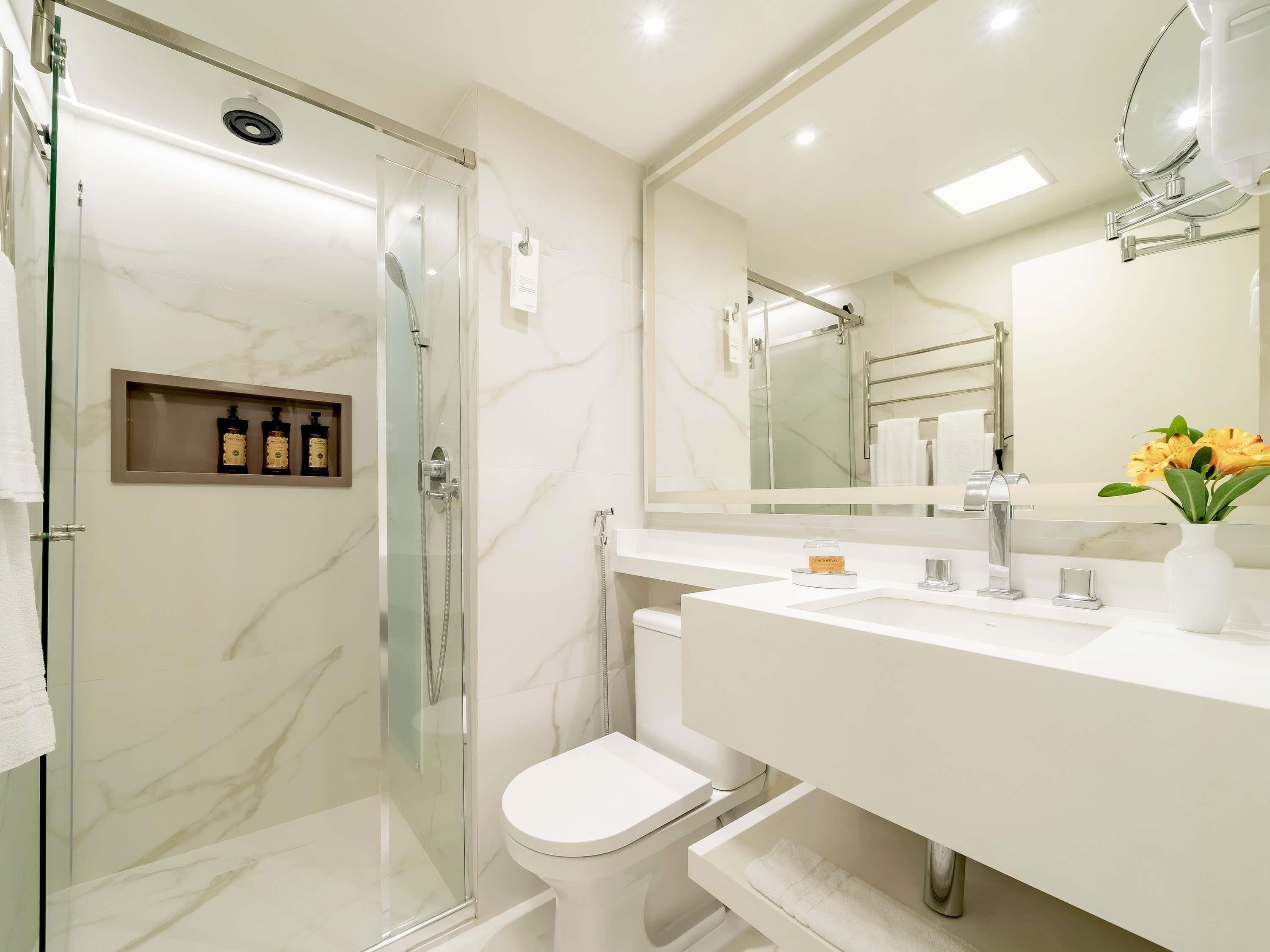 A modern bathroom with a glass-enclosed shower, a white toilet, a vanity with a mirror, and a vase with flowers.