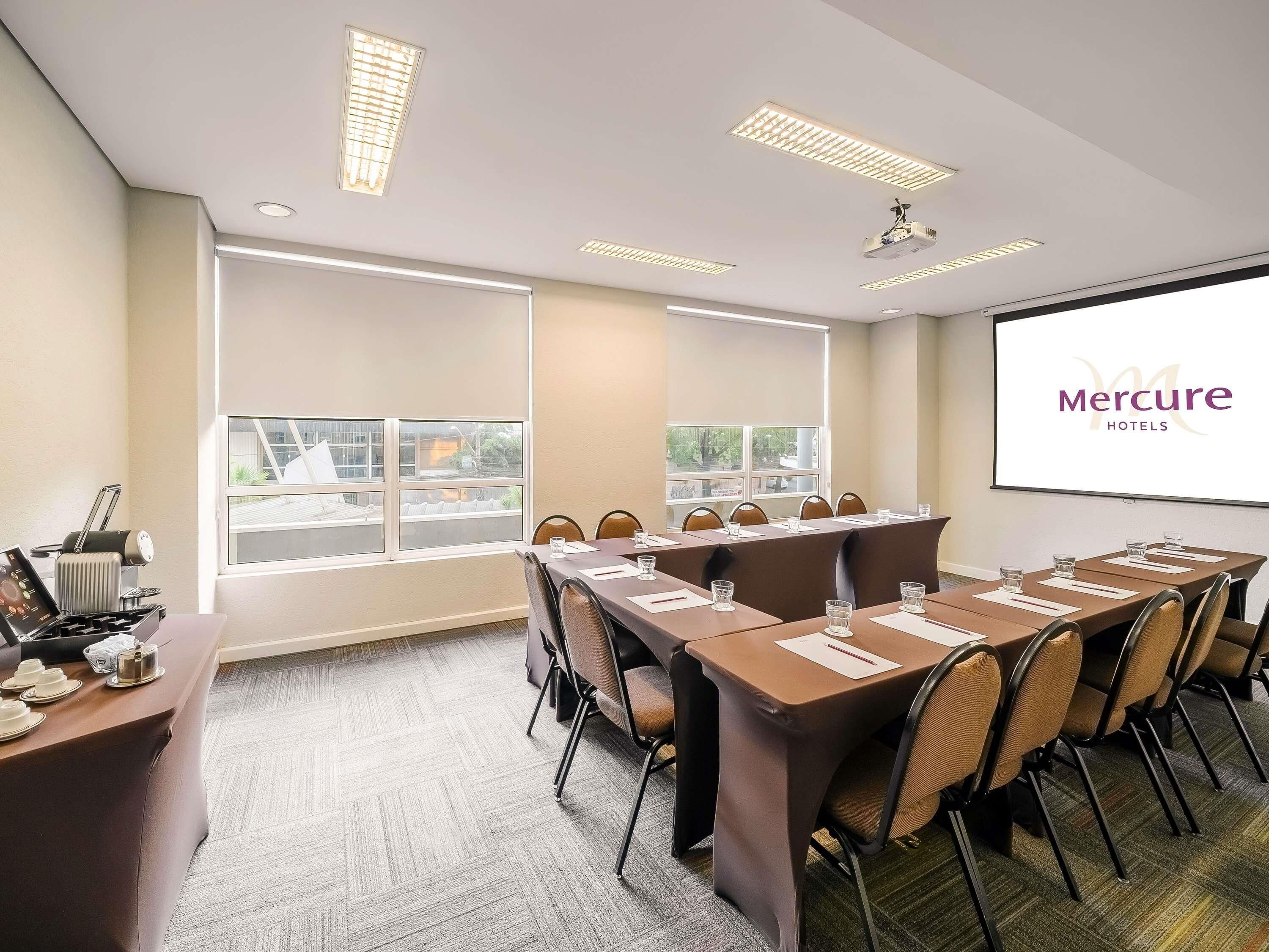 A conference room with a long table, chairs, a projector screen, and a window with a view.