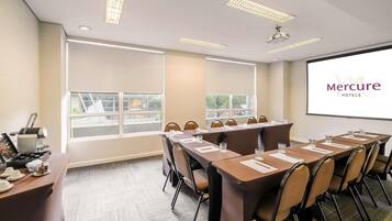 A conference room with a long table, chairs, a projector screen, and a window with a view.