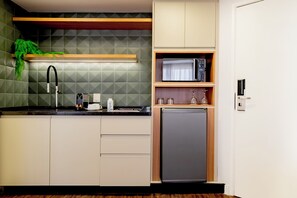 Una cocina compacta con microondas integrado, un lavamanos y un refrigerador pequeño.