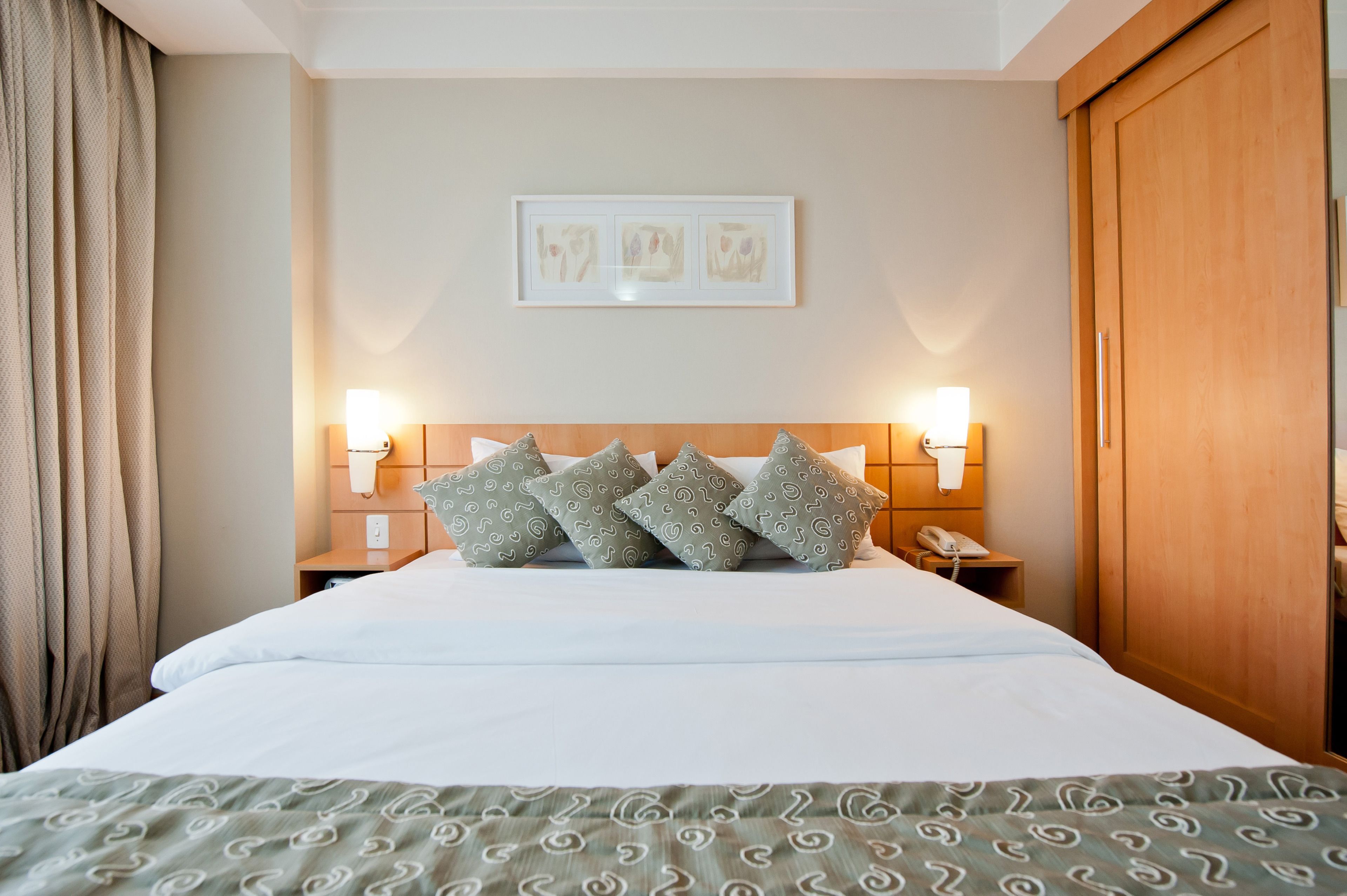 A hotel room with a bed, two bedside lamps, a telephone, and a framed artwork on the wall.