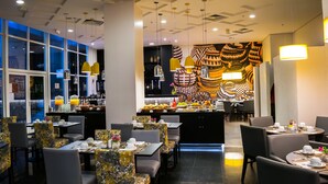 A restaurant with tables set for dining, a bar area, and a patterned wall in the background. - Mercure Guarulhos Aeroporto Hotel (Guarulhos)