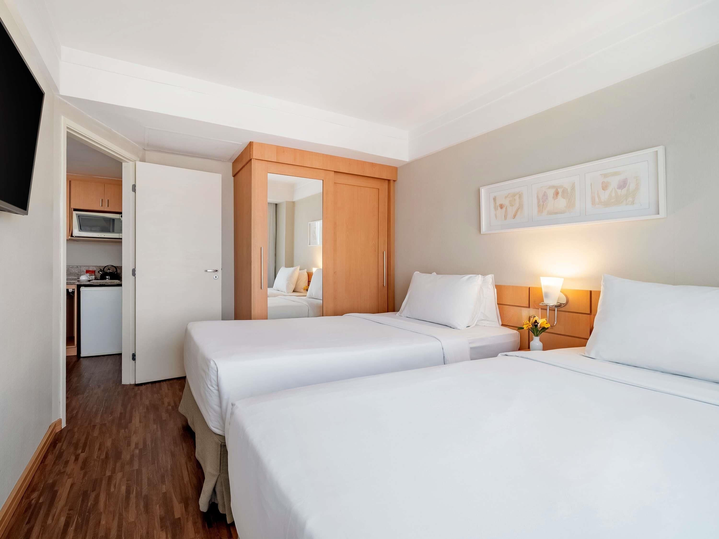 A hotel room with two beds, a small kitchenette, and a mirror.