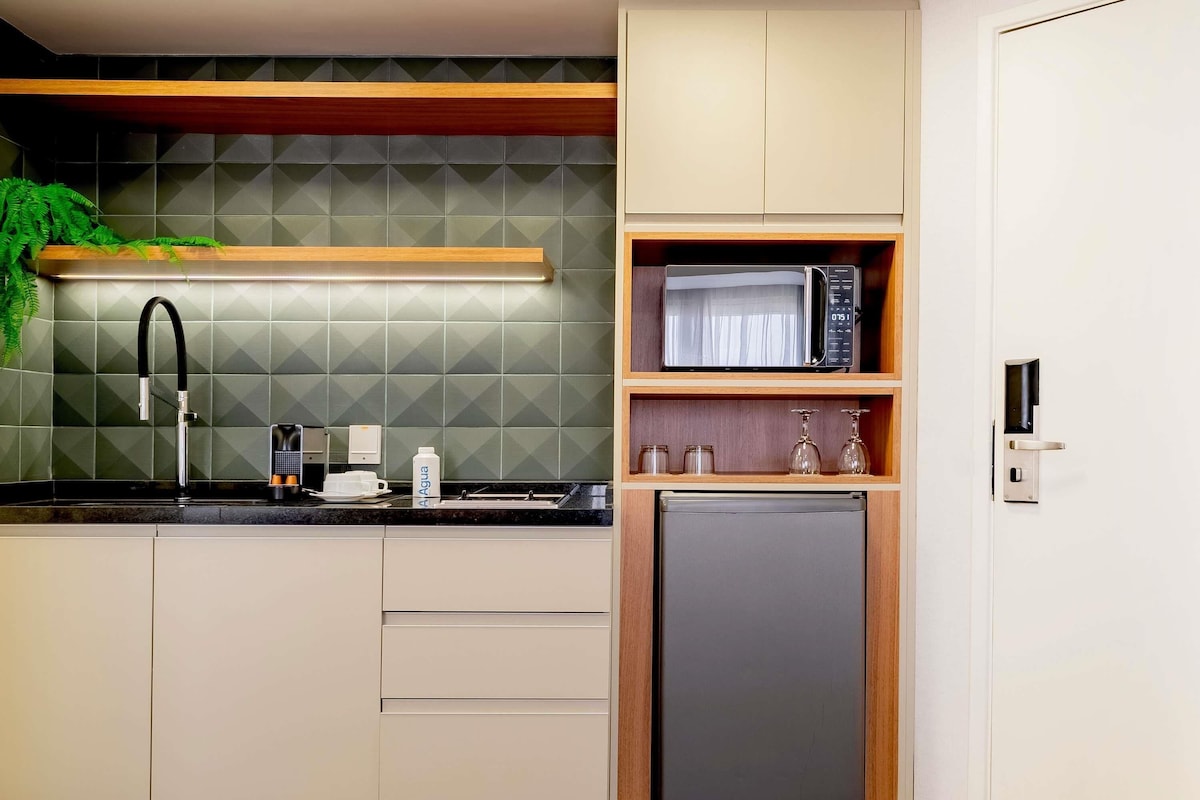 Una cocina compacta con microondas, refrigerador, pileta y una estantería con frascos y vasos.