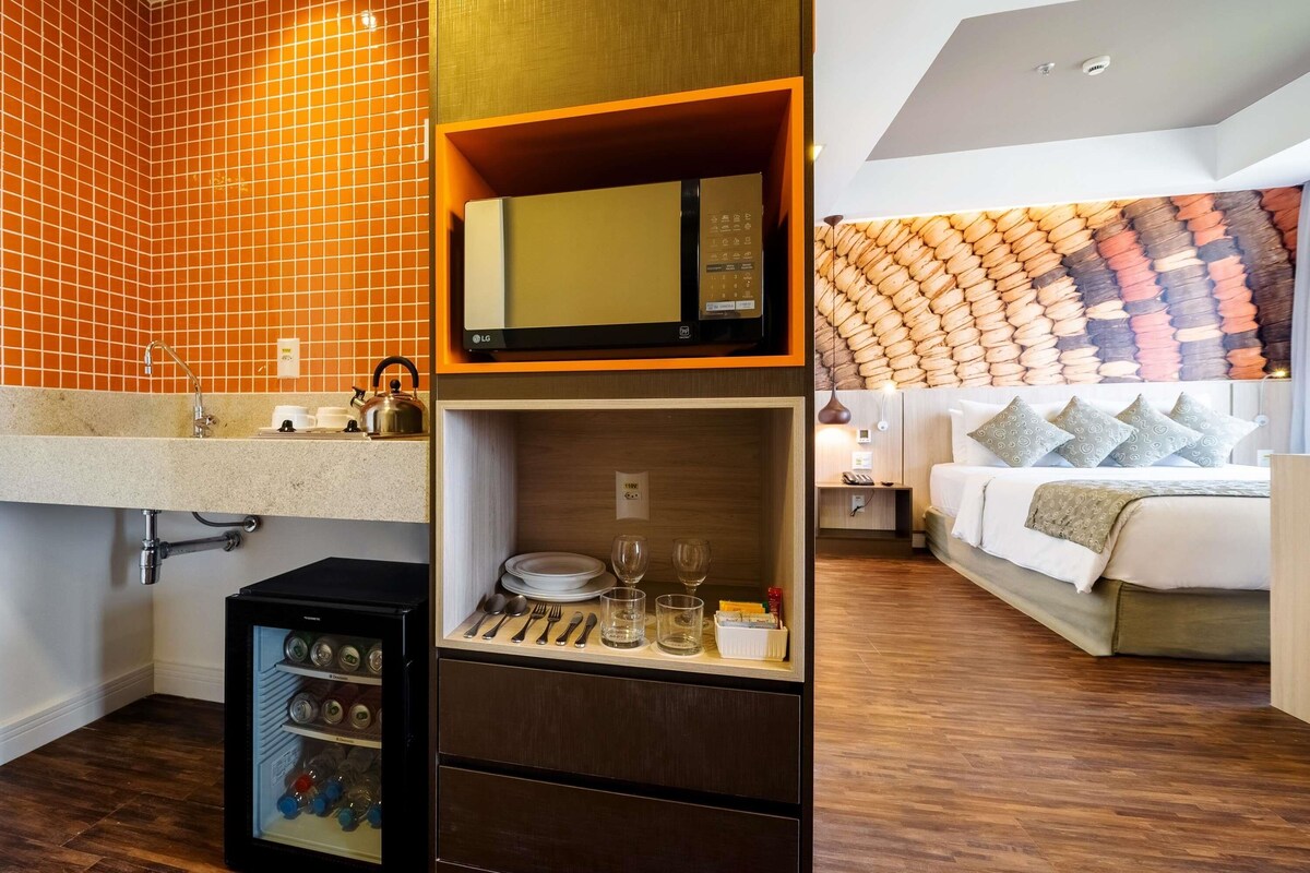 Habitación de hotel moderna con cocina, minibar y cama con cabecero estampado.