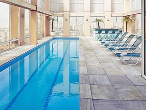 Une piscine à l’eau d’un bleu cristallin, entourée de chaises longues et offrant une vue sur le paysage urbain.