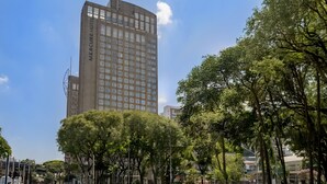 A tall building with the name 'Mercure Hotel' on its facade, surrounded by trees and other buildings. - Mercure Guarulhos Aeroporto Hotel (Guarulhos)