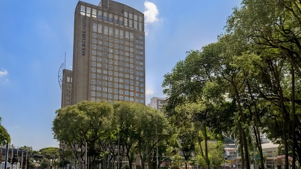 A tall building with the name 'Mercure Hotel' on its facade, surrounded by trees and other buildings. - Mercure Guarulhos Aeroporto Hotel (Guarulhos)