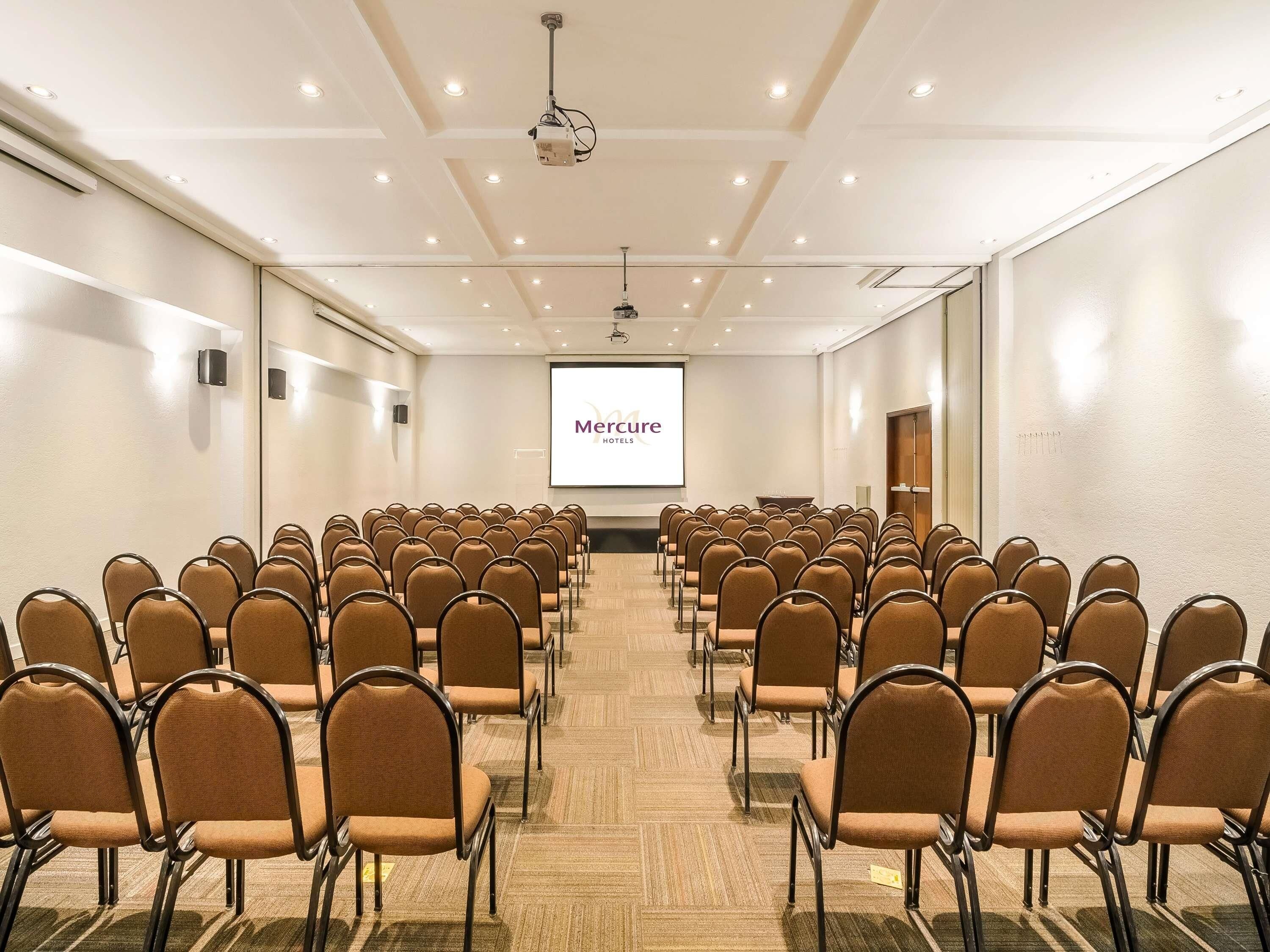 A conference room with rows of chairs, a projection screen, and a presentation on the screen.