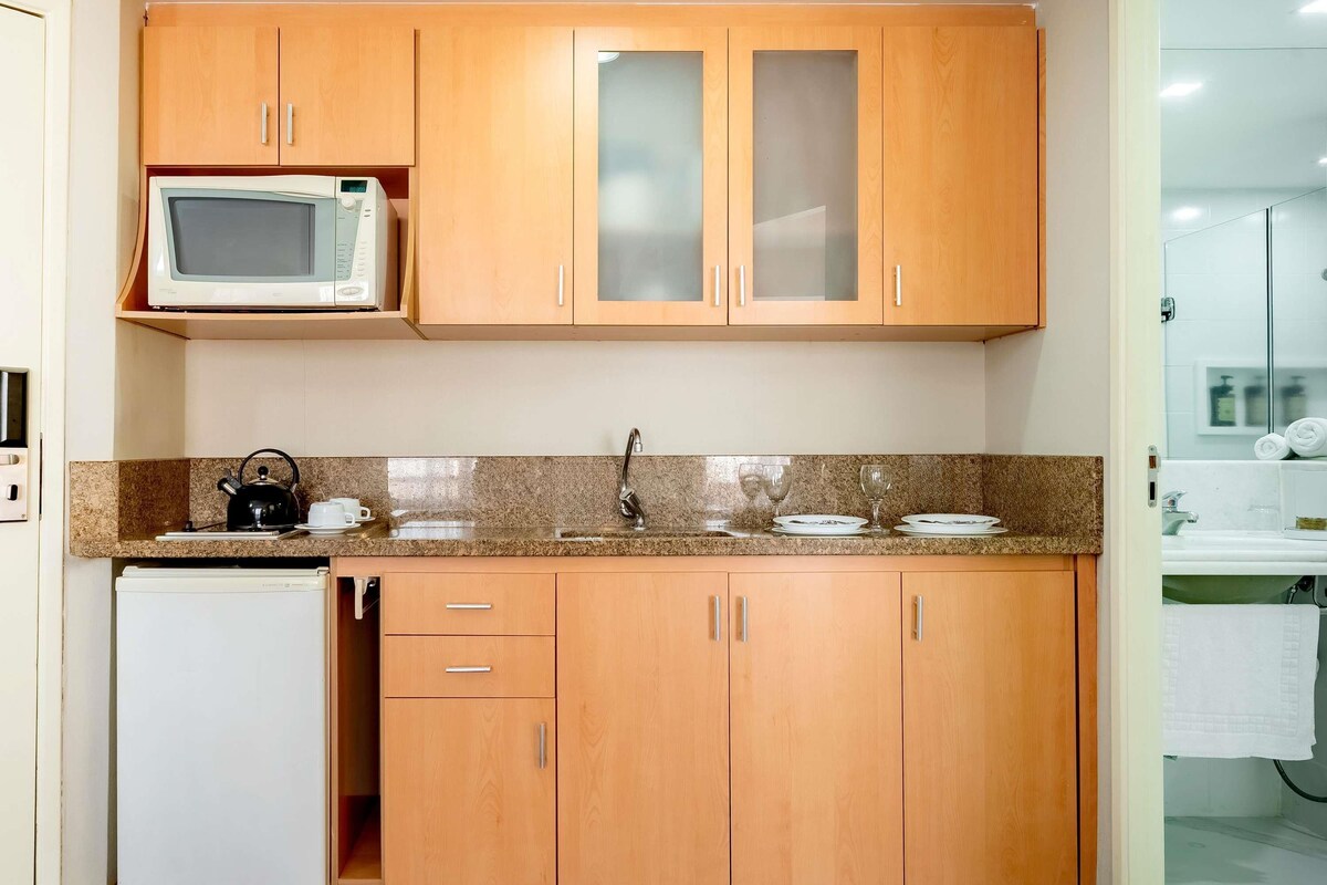Una cocina con armarios de madera, microondas, hervidor y refrigerador.